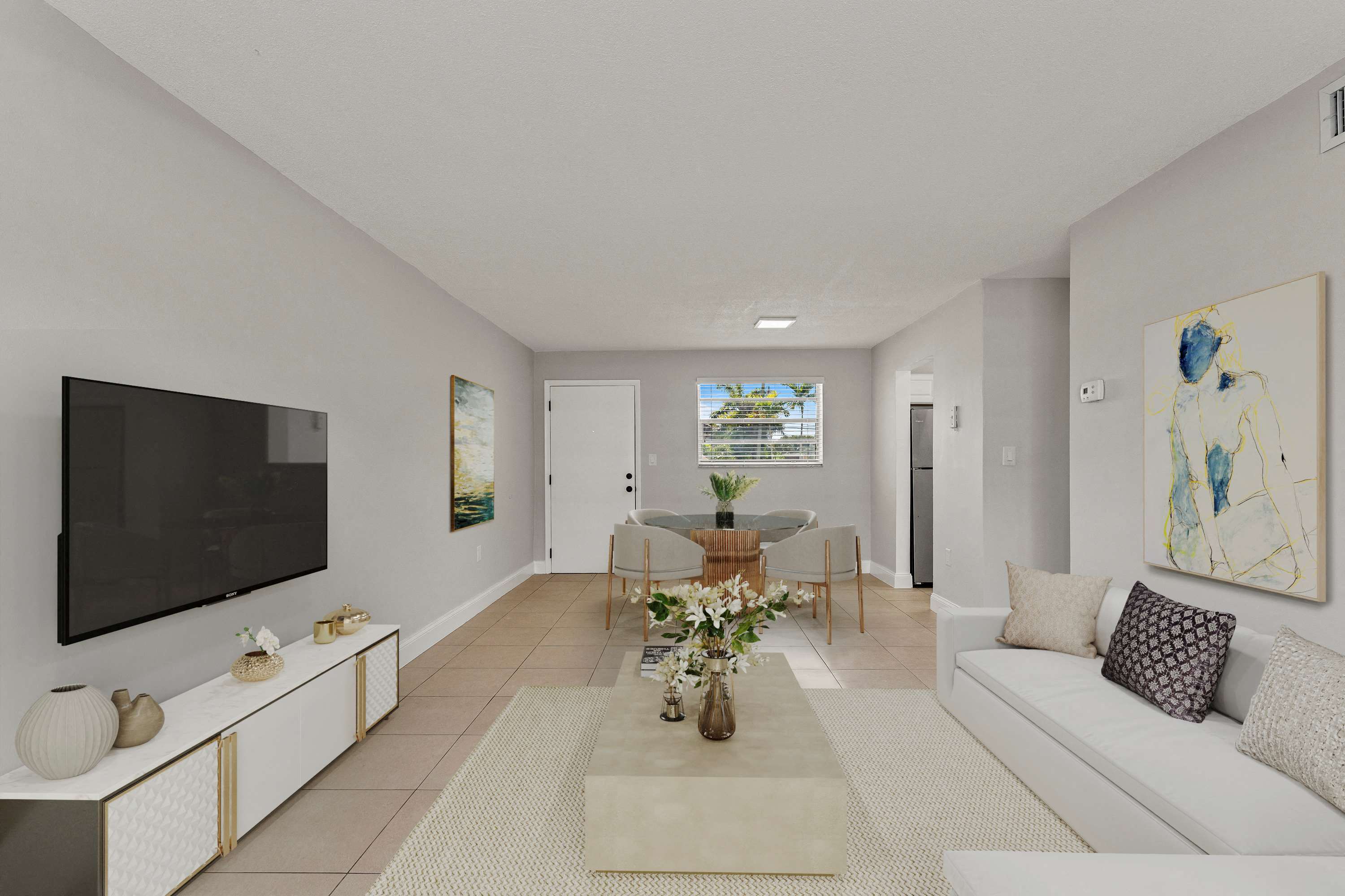 A living room with a flat screen TV on the left wall and a sofa with a throw pillow on the right.